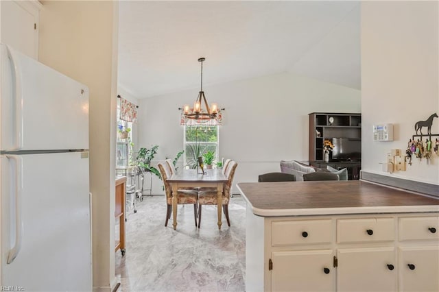 kitchen with a notable chandelier, vaulted ceiling, white cabinetry, freestanding refrigerator, and decorative light fixtures