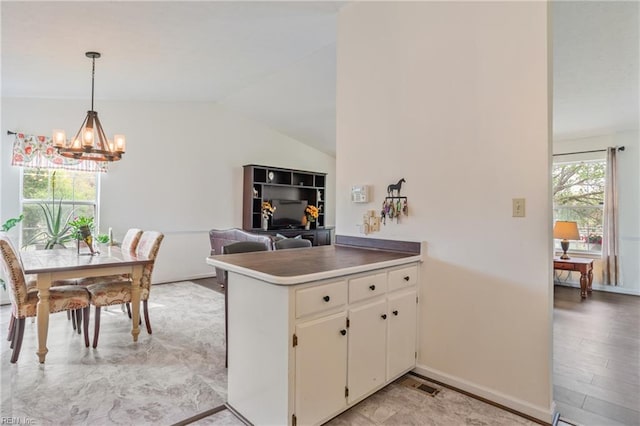 kitchen with hanging light fixtures, a notable chandelier, a peninsula, white cabinetry, and vaulted ceiling