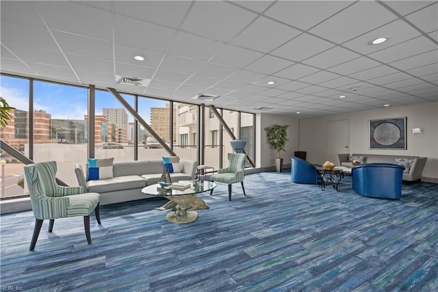 carpeted living room featuring visible vents, baseboards, a view of city, a drop ceiling, and expansive windows