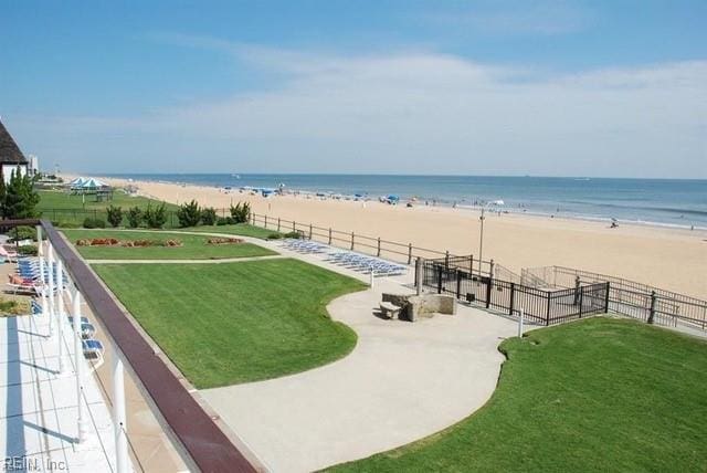 surrounding community with a water view, fence, a yard, and a view of the beach