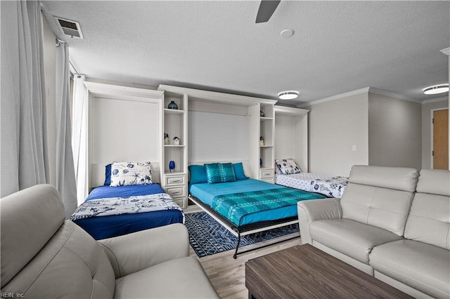 bedroom featuring visible vents, a textured ceiling, crown molding, and wood finished floors