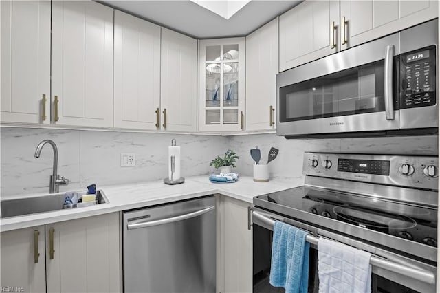kitchen featuring glass insert cabinets, white cabinetry, appliances with stainless steel finishes, a sink, and backsplash