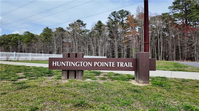 community sign featuring fence, a lawn, and a forest view