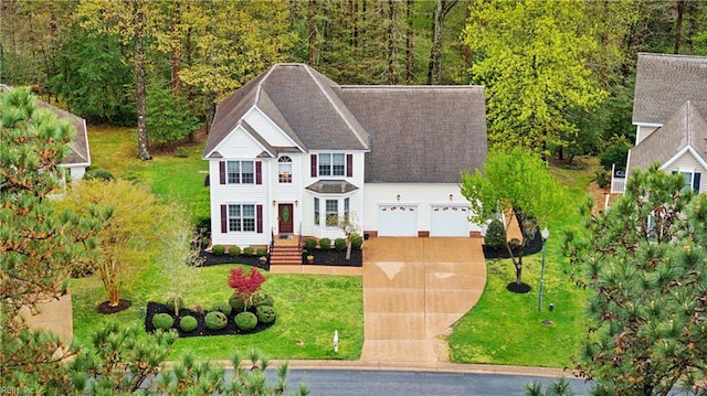 colonial home with a front yard, a wooded view, an attached garage, concrete driveway, and roof with shingles