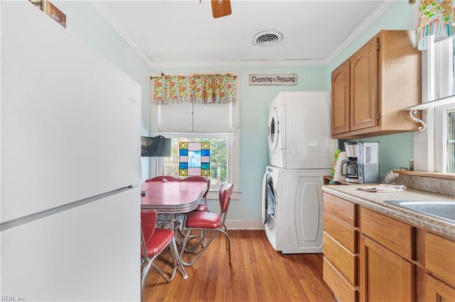 kitchen featuring visible vents, ornamental molding, freestanding refrigerator, stacked washer / dryer, and light wood finished floors