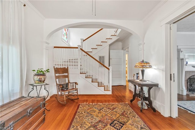 foyer entrance with arched walkways, wood finished floors, crown molding, and stairs