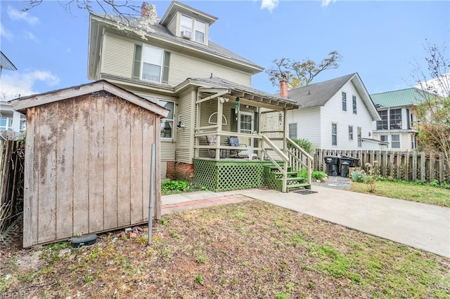 back of house with a storage unit, fence, an outbuilding, and covered porch