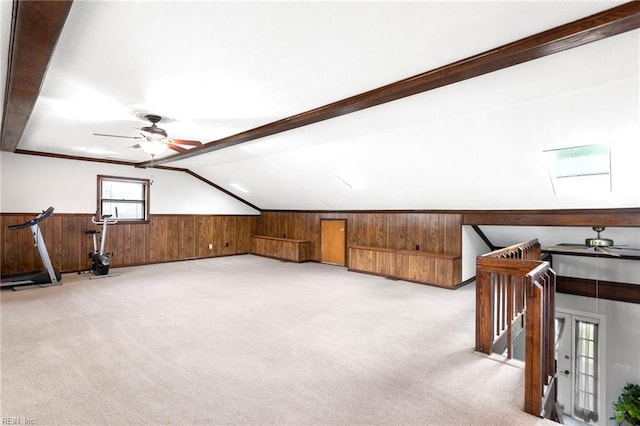 additional living space with vaulted ceiling with skylight, wooden walls, light colored carpet, and a ceiling fan