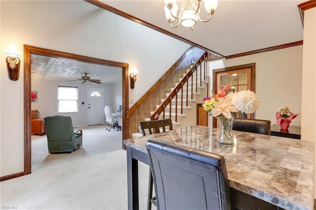 carpeted dining room featuring ceiling fan with notable chandelier, baseboards, ornamental molding, and stairs