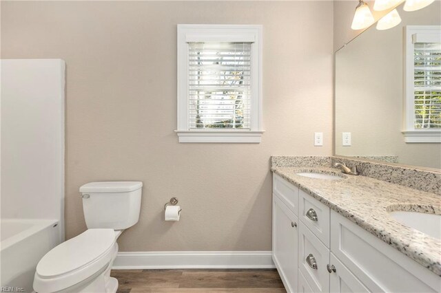 full bath with toilet, wood finished floors, double vanity, and baseboards
