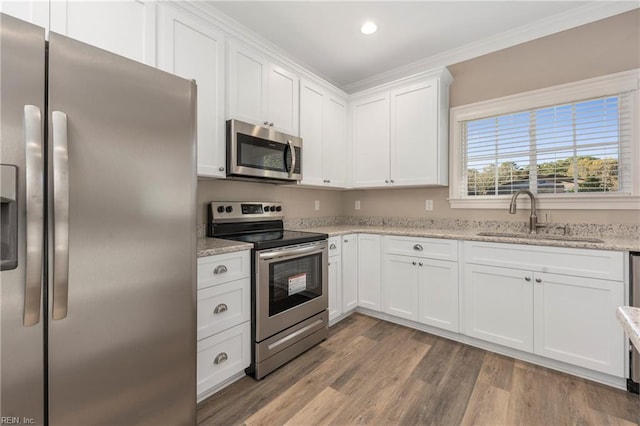 kitchen featuring white cabinets, a sink, ornamental molding, appliances with stainless steel finishes, and light wood-style flooring