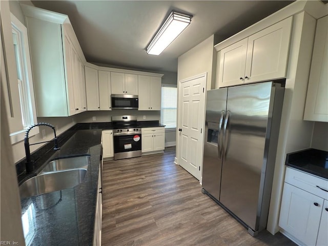 kitchen featuring dark wood-style flooring, white cabinets, dark stone counters, stainless steel appliances, and a sink