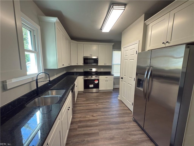 kitchen featuring dark stone counters, dark wood finished floors, white cabinets, a sink, and stainless steel appliances
