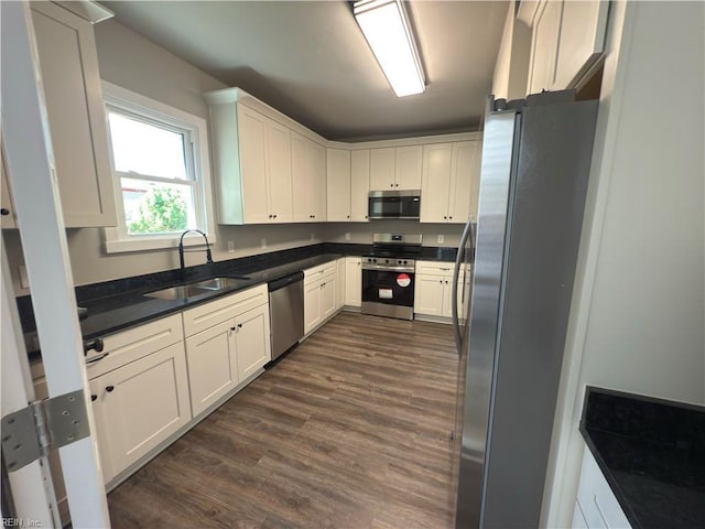 kitchen with white cabinets, a sink, dark countertops, dark wood-style floors, and stainless steel appliances
