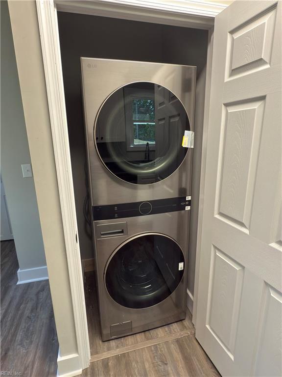 clothes washing area featuring baseboards, stacked washer and dryer, laundry area, and wood finished floors