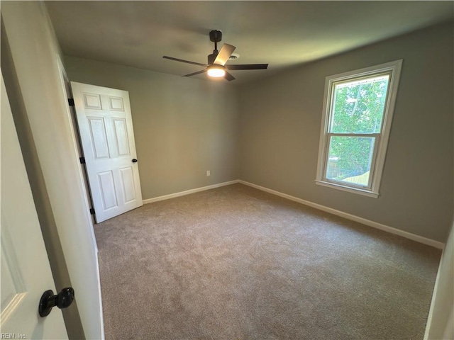 carpeted spare room featuring baseboards and a ceiling fan