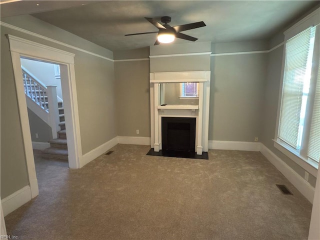 unfurnished living room with a fireplace with flush hearth, a ceiling fan, visible vents, carpet flooring, and stairs