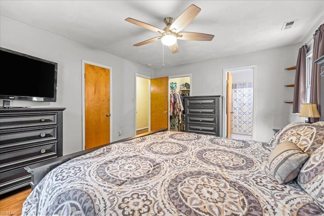 bedroom with a closet, ensuite bathroom, a walk in closet, visible vents, and wood finished floors