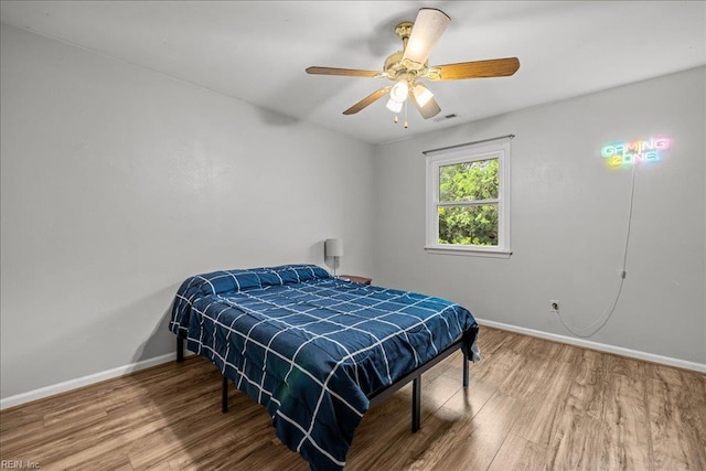 bedroom featuring ceiling fan, visible vents, baseboards, and wood finished floors