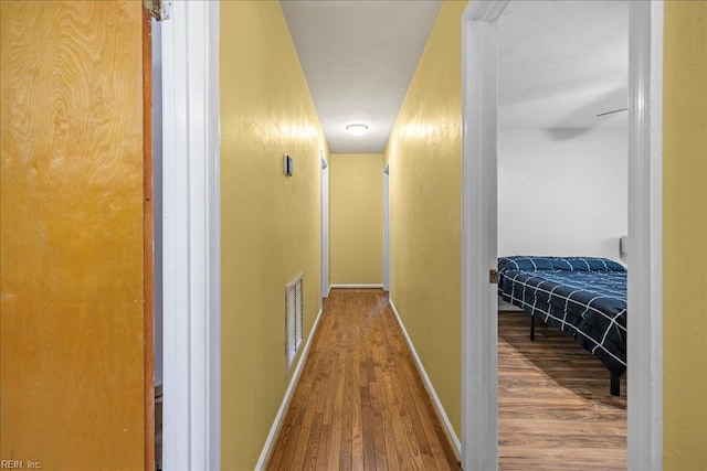 corridor featuring wood finished floors, baseboards, and visible vents