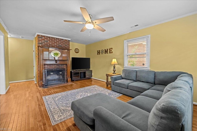 living room featuring crown molding, ceiling fan, visible vents, wood finished floors, and baseboards