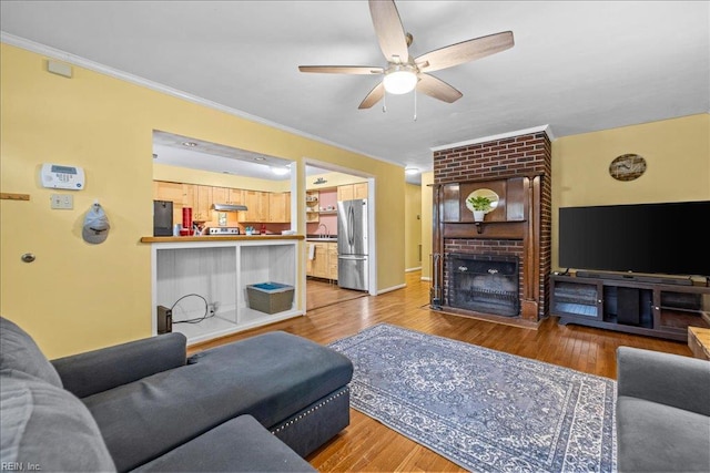 living area featuring baseboards, ornamental molding, a fireplace, a ceiling fan, and wood finished floors