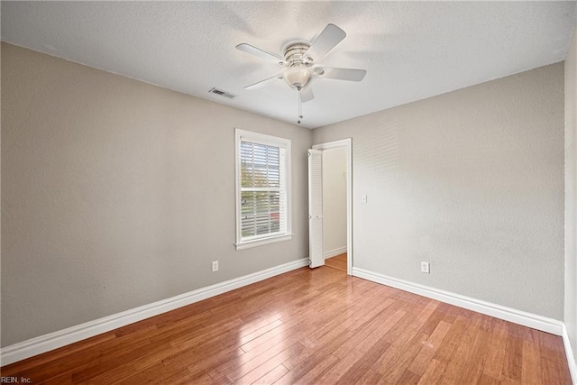 spare room with a textured ceiling, a ceiling fan, visible vents, wood-type flooring, and baseboards