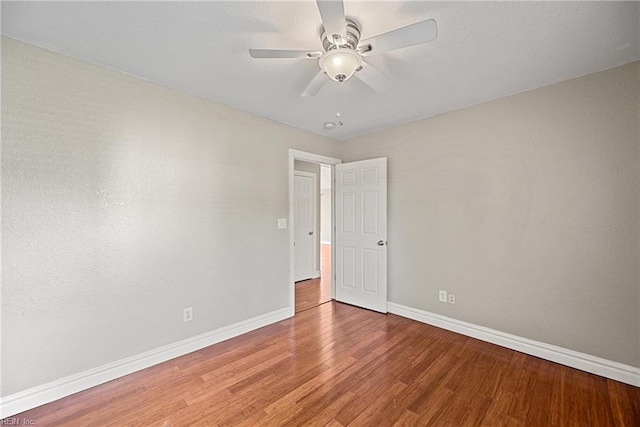 empty room featuring wood finished floors, baseboards, and a ceiling fan