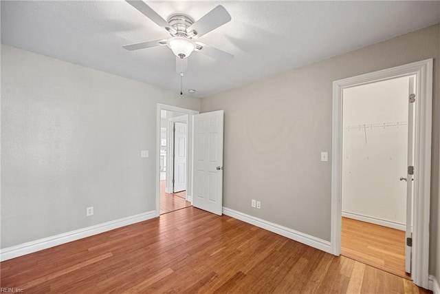 unfurnished bedroom featuring light wood-type flooring, a closet, baseboards, and a walk in closet