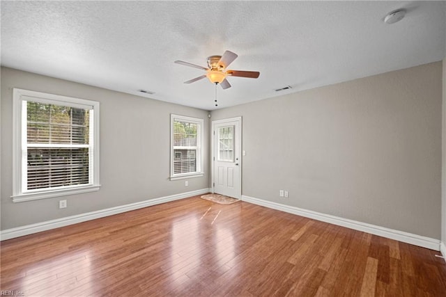 spare room featuring ceiling fan, a textured ceiling, visible vents, wood finished floors, and baseboards