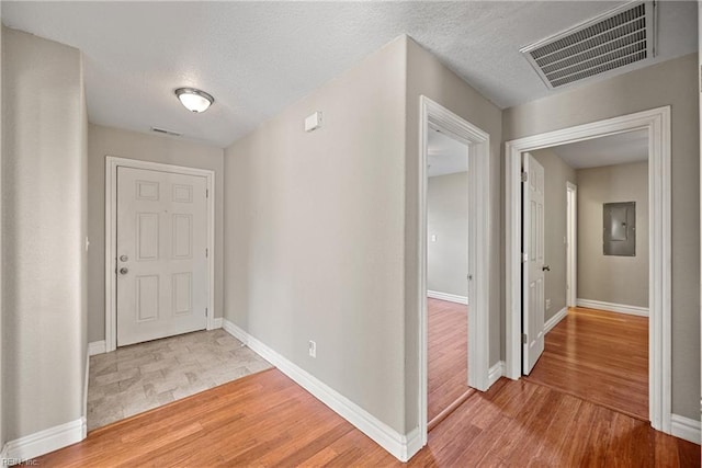 hall with a textured ceiling, light wood finished floors, baseboards, and visible vents
