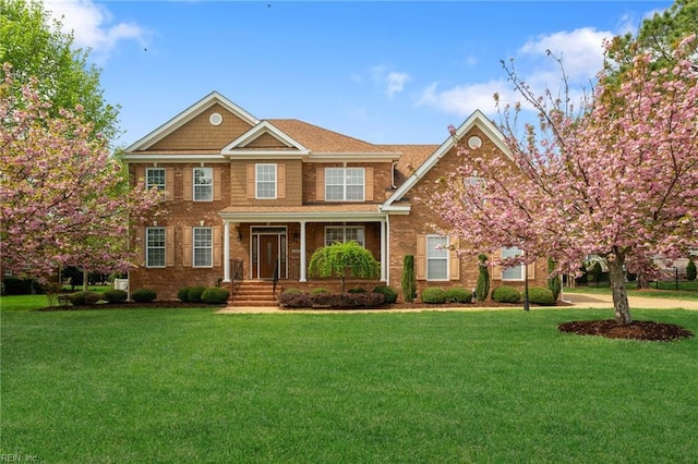 view of front of property with covered porch, a front lawn, and brick siding