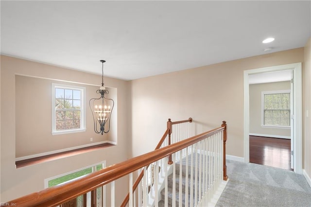 corridor featuring an upstairs landing, carpet flooring, a notable chandelier, and a healthy amount of sunlight