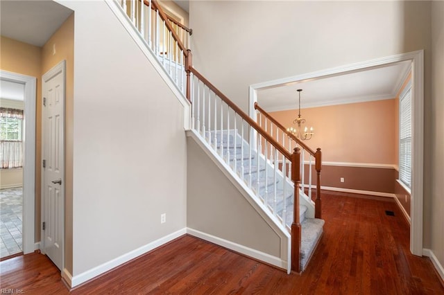 stairs featuring a notable chandelier, baseboards, crown molding, visible vents, and wood finished floors