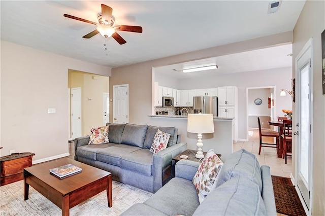 living area featuring light tile patterned floors, ceiling fan, and baseboards