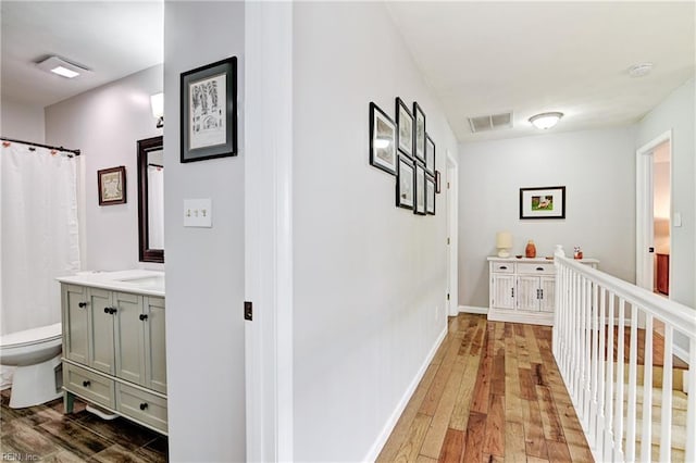corridor with wood-type flooring, visible vents, and baseboards