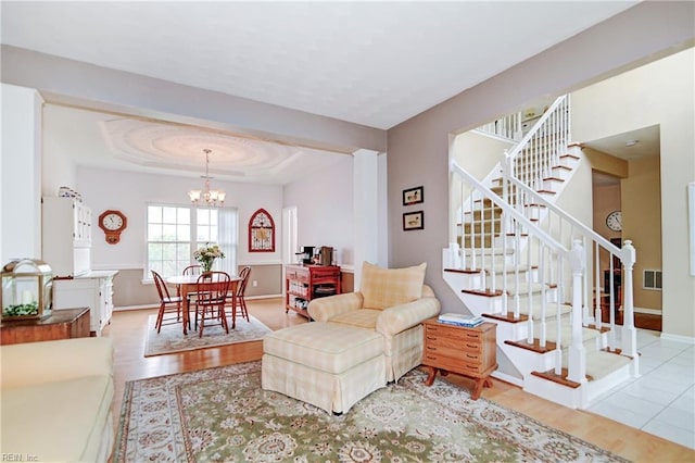 living room with visible vents, stairway, a chandelier, wood finished floors, and a raised ceiling