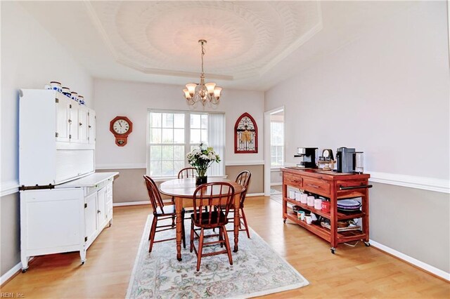 dining space with a tray ceiling, light wood-style floors, an inviting chandelier, and baseboards