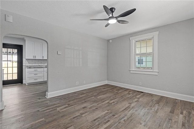 unfurnished room with baseboards, arched walkways, dark wood-style flooring, ceiling fan, and a textured ceiling