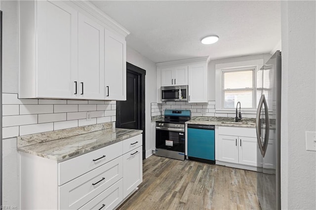 kitchen with a sink, white cabinets, appliances with stainless steel finishes, and light wood-style floors