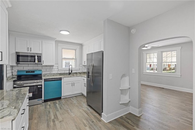kitchen with white cabinets, a sink, appliances with stainless steel finishes, light stone countertops, and decorative backsplash
