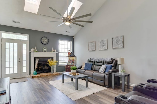 living room with high vaulted ceiling, ceiling fan, visible vents, a skylight, and wood finished floors