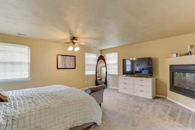 bedroom with a glass covered fireplace, baseboards, visible vents, ceiling fan, and light colored carpet