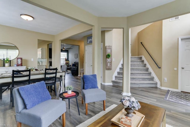 living room with stairs, visible vents, wood finished floors, and ceiling fan