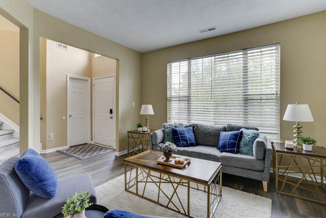 living room featuring wood finished floors, baseboards, visible vents, and stairway