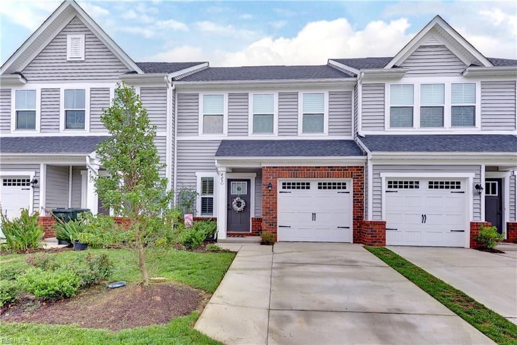 townhome / multi-family property with brick siding, an attached garage, driveway, and roof with shingles