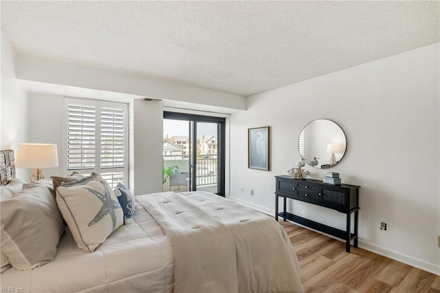 bedroom with access to exterior, light wood-type flooring, baseboards, and a textured ceiling