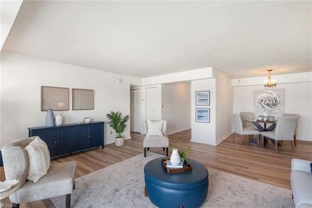 living area with light wood-style floors, baseboards, and an inviting chandelier