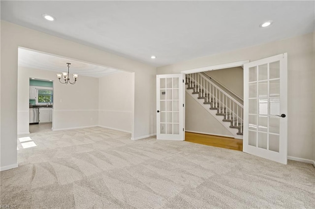 spare room featuring a notable chandelier, stairway, french doors, and light colored carpet