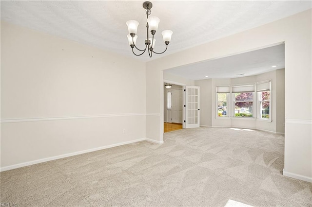 spare room with carpet, french doors, baseboards, and an inviting chandelier